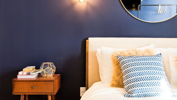 Une chambre à coucher avec un lit, une table de chevet et un miroir fixé au mur.