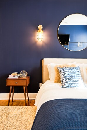 Un dormitorio con cama, mesita de noche y espejo montado en la pared.