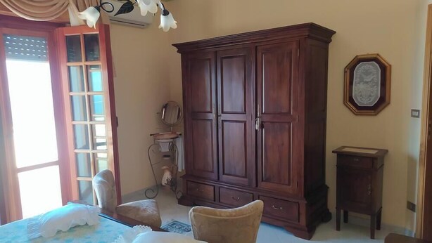 Een kamer met een grote houten garderobe, een bed met een witte dekbedovertrek, een klein rond tafeltje en een spiegel aan de muur.