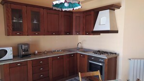 Een kleine keuken met houten kastjes, een magnetron, een koffieapparaat, een gasfornuis en een spoelbak.