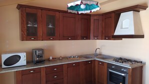 Een keuken met houten kastjes, een magnetron, een koffiezetapparaat, een spoelbak en een fornuis.