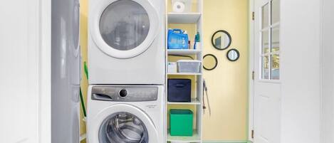 A compact laundry room with two stacked washing machines, a shelf with cleaning supplies, and a small storage unit.