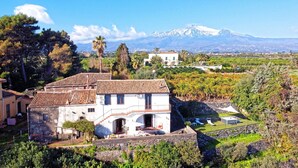 Une villa avec un toit en tuiles, un mur en pierre et un jardin agrémenté d’un espace salon extérieur.