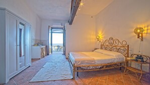 Une chambre à coucher avec un lit, une table de chevet, une lampe et une vue sur la mer, visible par une porte ouverte.