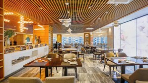 Un restaurante moderno con paneles de techo de madera, una zona de buffet y vistas a la ciudad a través de amplios ventanales.