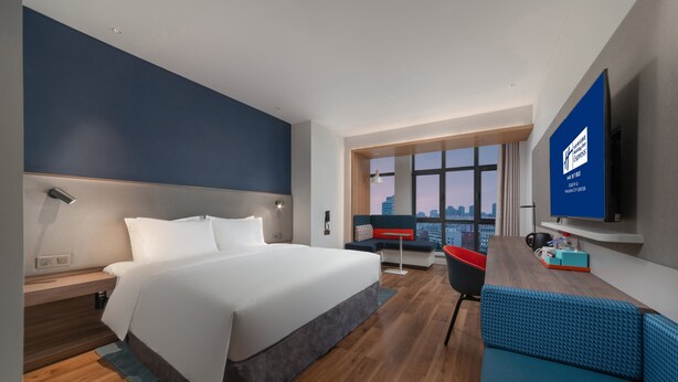 Una habitación de hotel moderna con una cama grande, un área de estar, un televisor y vista a la ciudad.