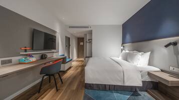 A modern hotel room with a bed, desk, chair, and a large flat-screen TV.