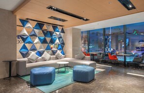 A modern lobby with a geometric wall design, a seating area with a sofa and ottomans, and a view of the city through large windows. - Holiday Inn Express Yangquan City Center by IHG (Yangquan)