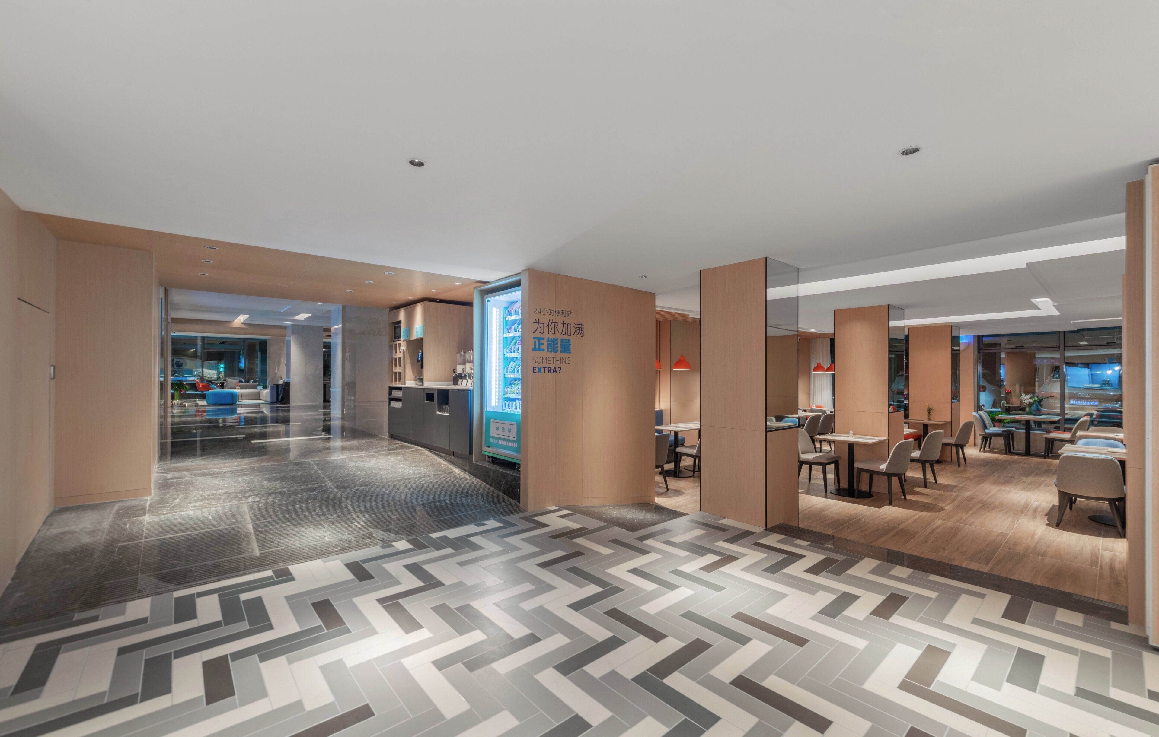 Eine moderne Hotelhalle mit einem Fischgrätparkett, einem Empfangstisch und einer Sitzecke mit Tischen und Stühlen.