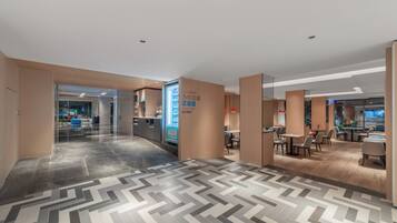 Eine moderne Hotelhalle mit einem Fischgrätparkett, einem Empfangstisch und einer Sitzecke mit Tischen und Stühlen.