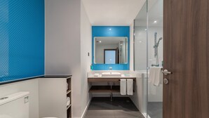 Un baño moderno con cabina de ducha de vidrio, inodoro blanco y lavamanos con resalte azul.