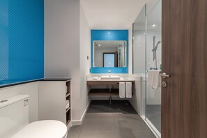 Un baño moderno con cabina de ducha de vidrio, inodoro blanco y lavamanos con resalte azul.