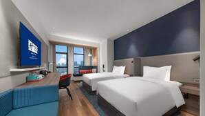 Una habitación de hotel moderna con dos camas, un sofá, un televisor y vistas a la ciudad.