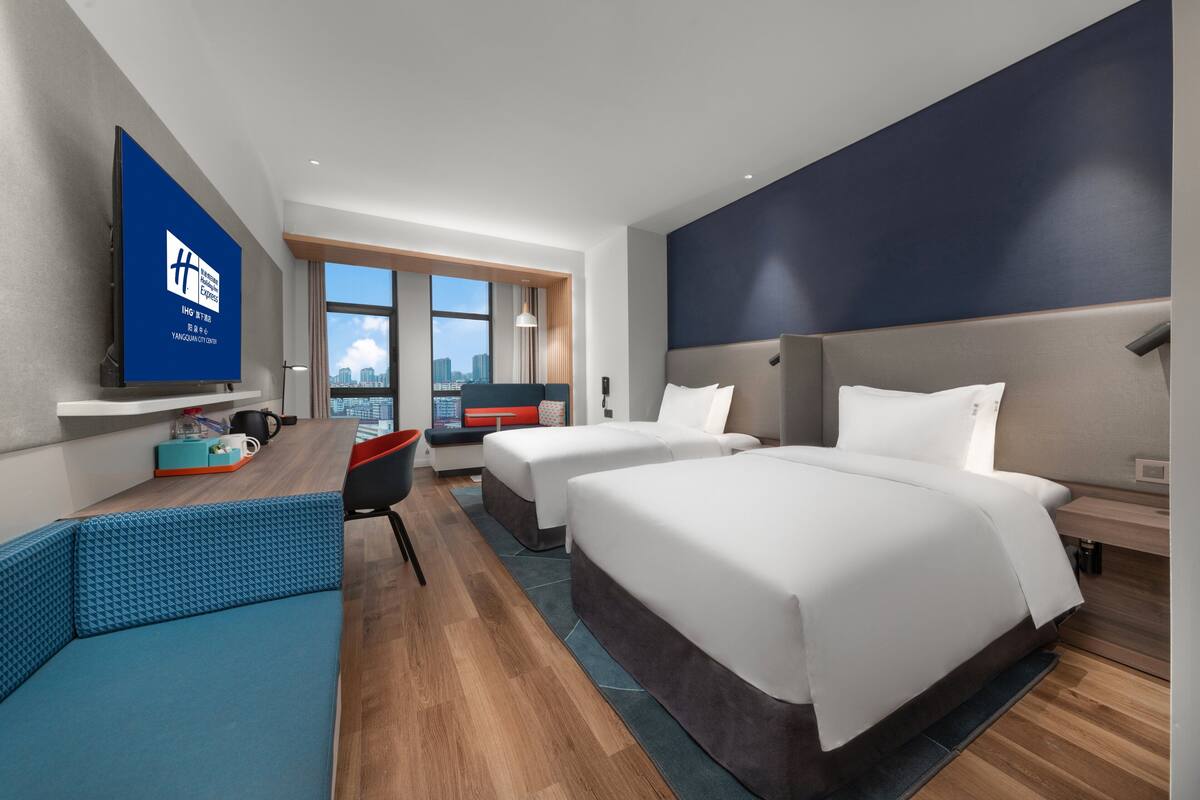 A modern hotel room with two beds, a sofa, a TV, and a city view.