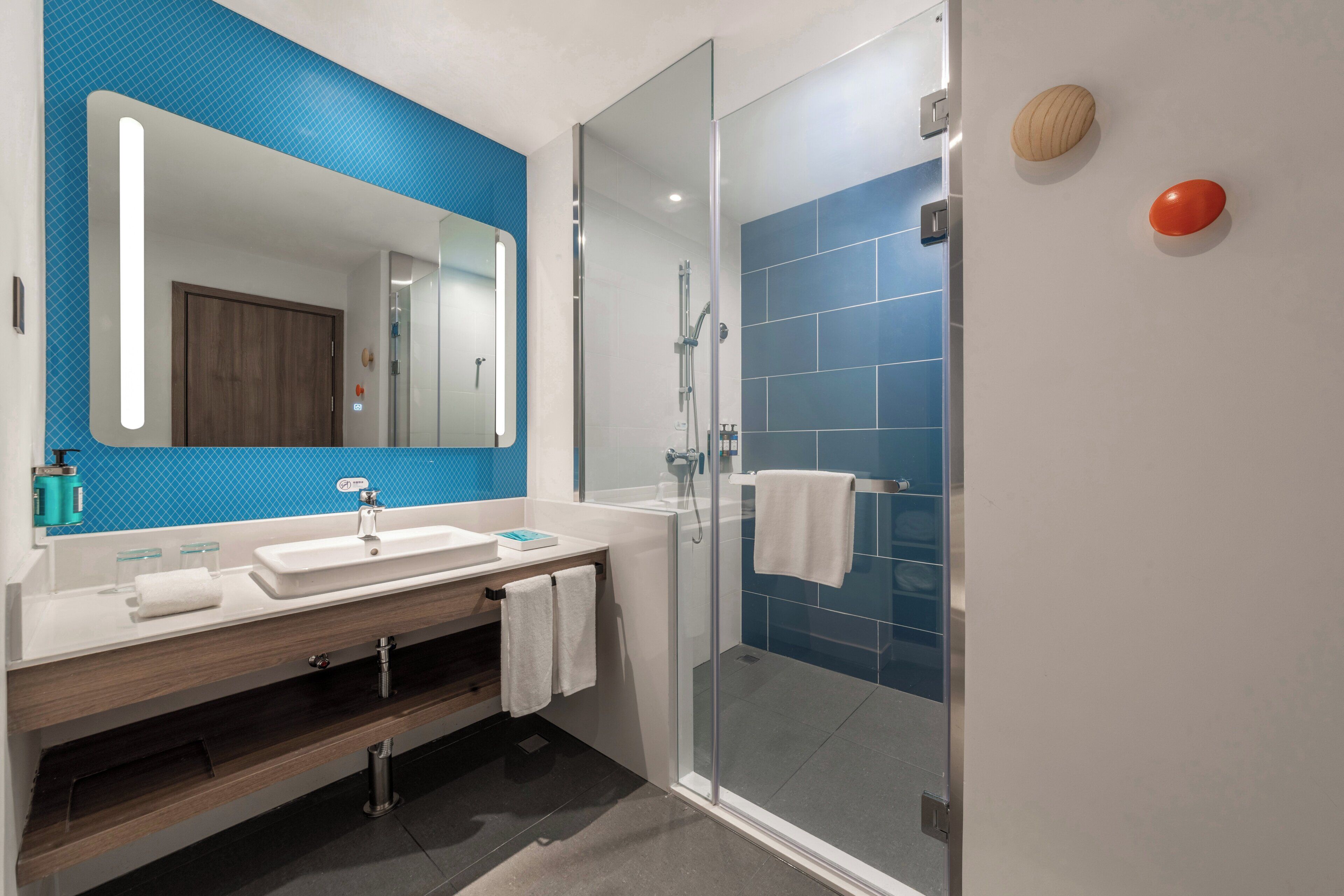 A modern bathroom with a glass shower enclosure, a large mirror, and a vanity with a sink and towel rack.