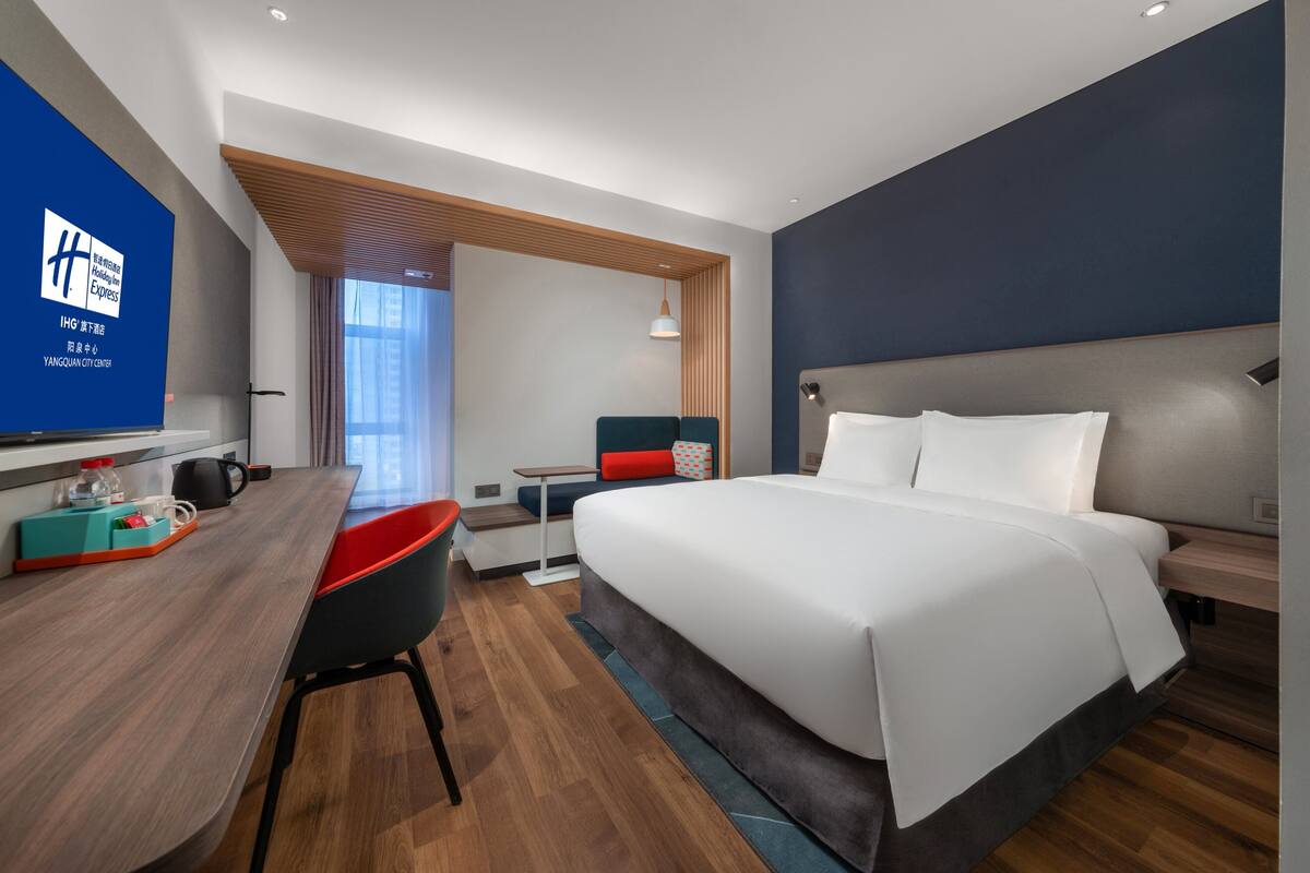 A modern hotel room with a large bed, a desk, and a seating area.