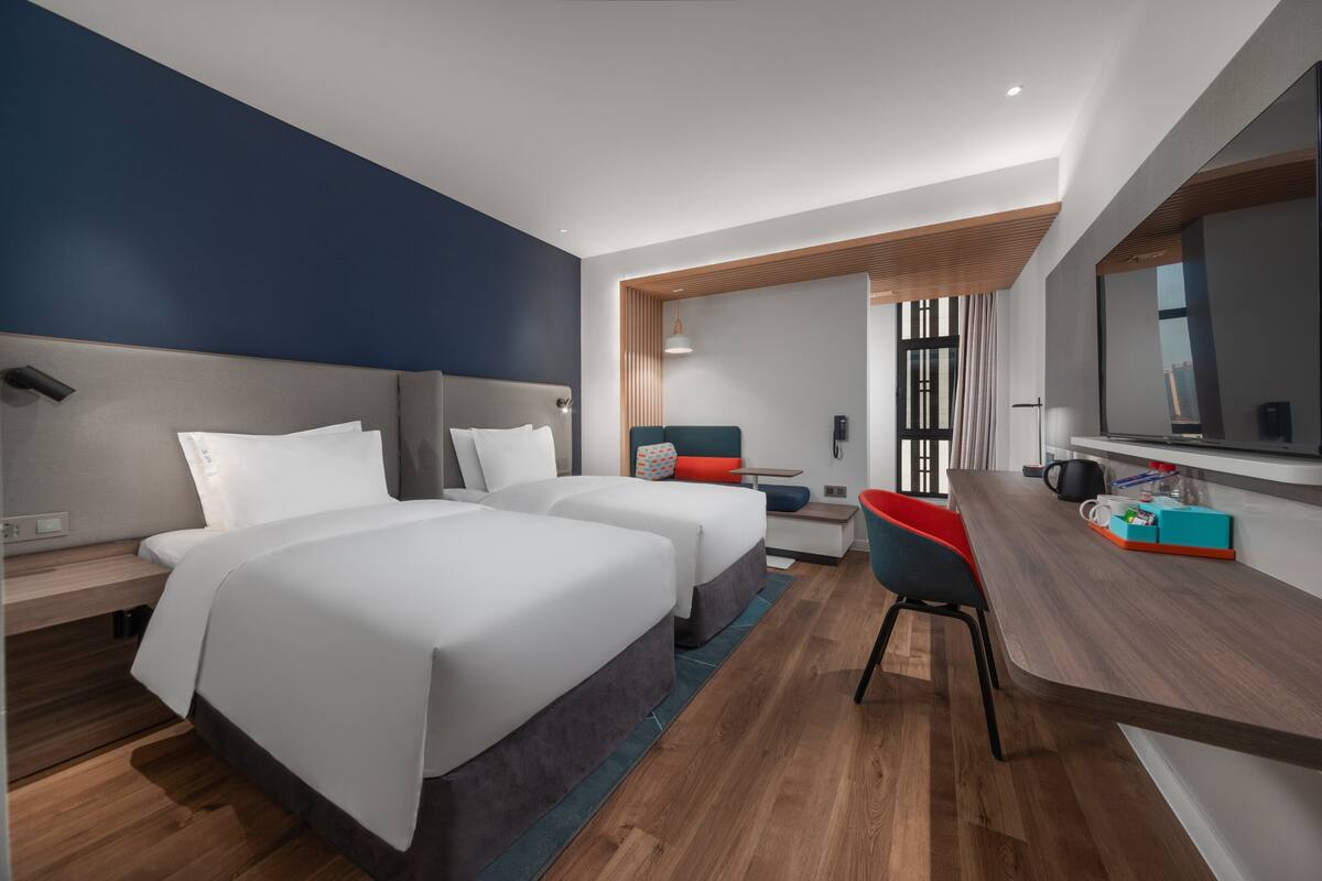 Ein modernes Hotelzimmer mit zwei Betten, einem Schreibtisch und einer Sitzecke.