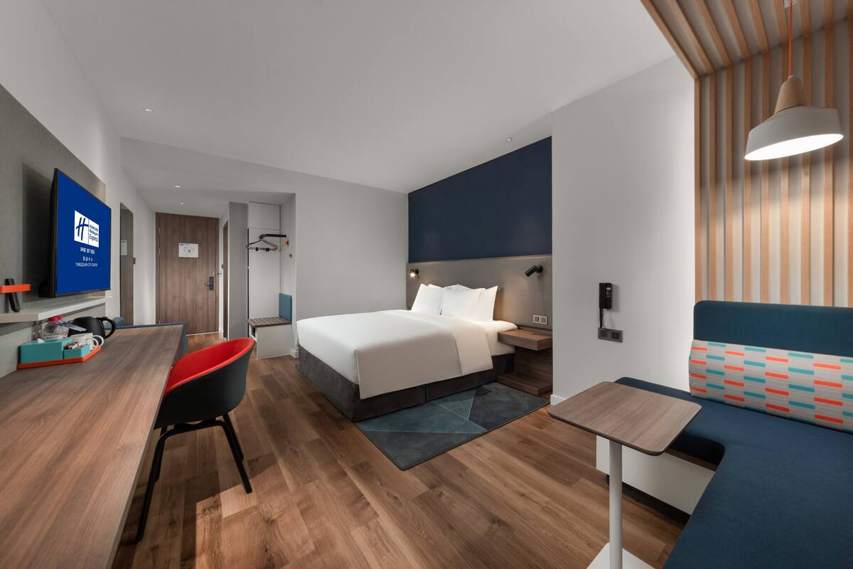 A modern hotel room with a bed, a desk, a chair, a TV, and a sofa.