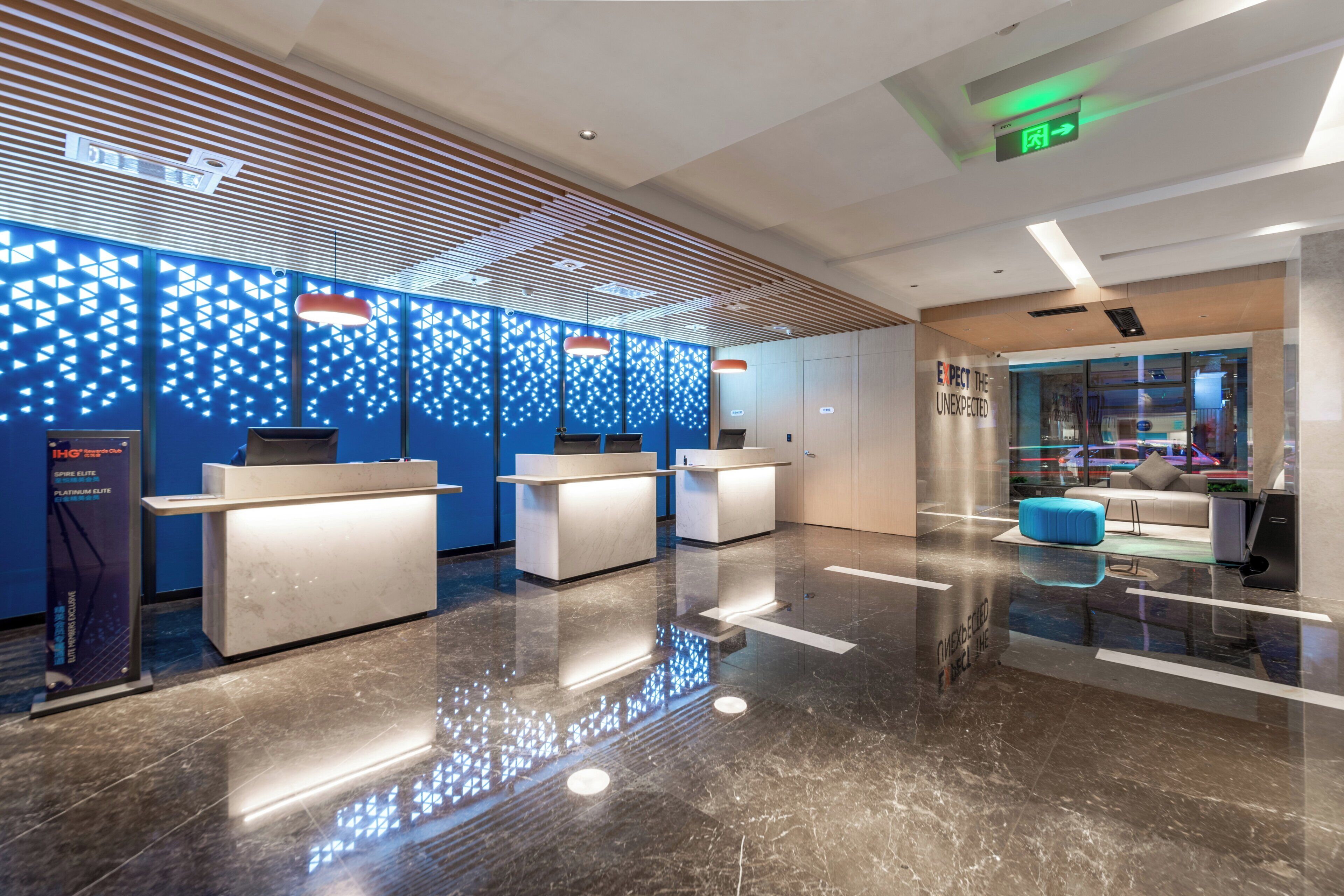 A modern reception area with a blue patterned wall, a reception desk, a seating area with a blue sofa, and a glass partition.