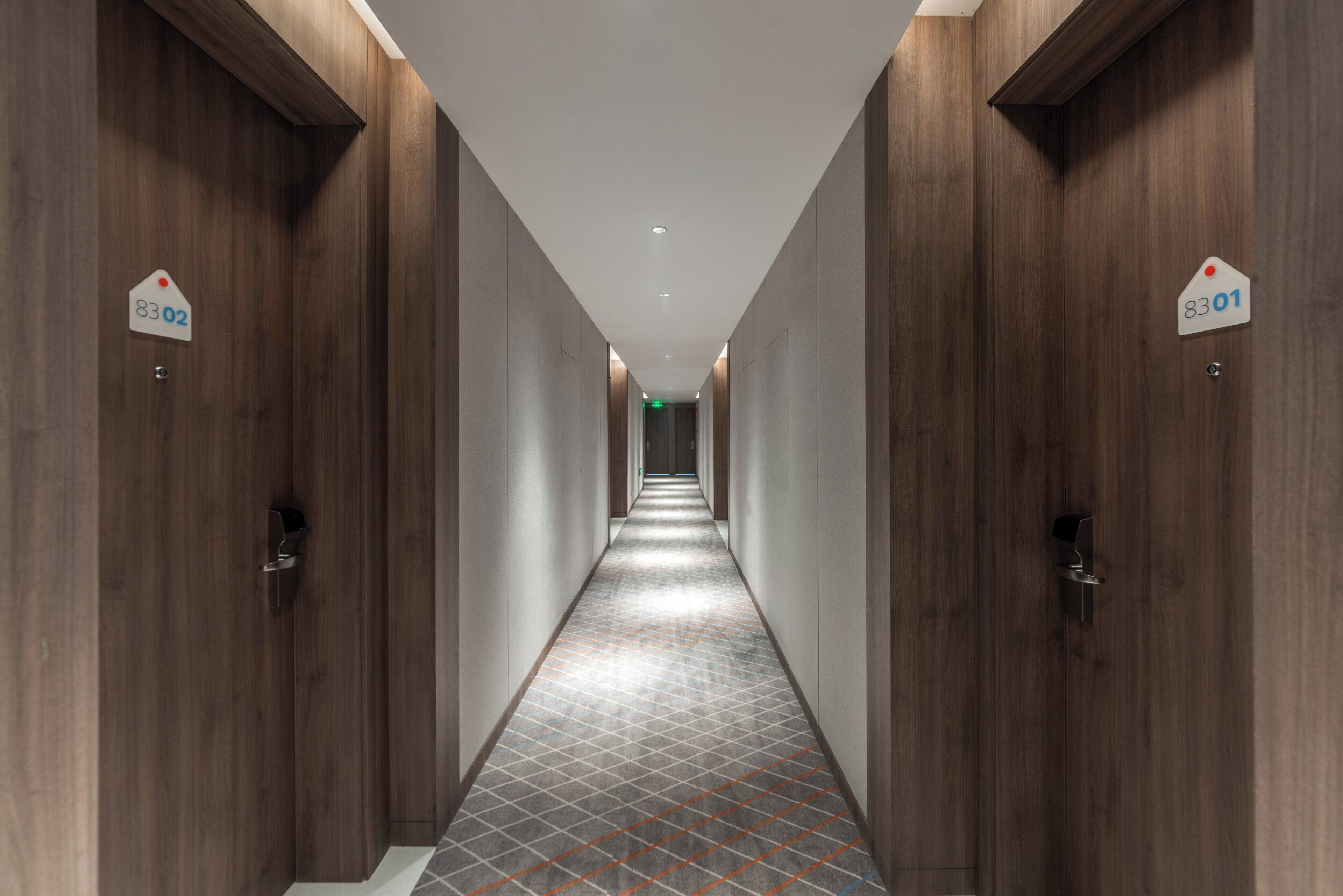 A hotel corridor with wooden doors, numbered room signs, and a patterned floor.