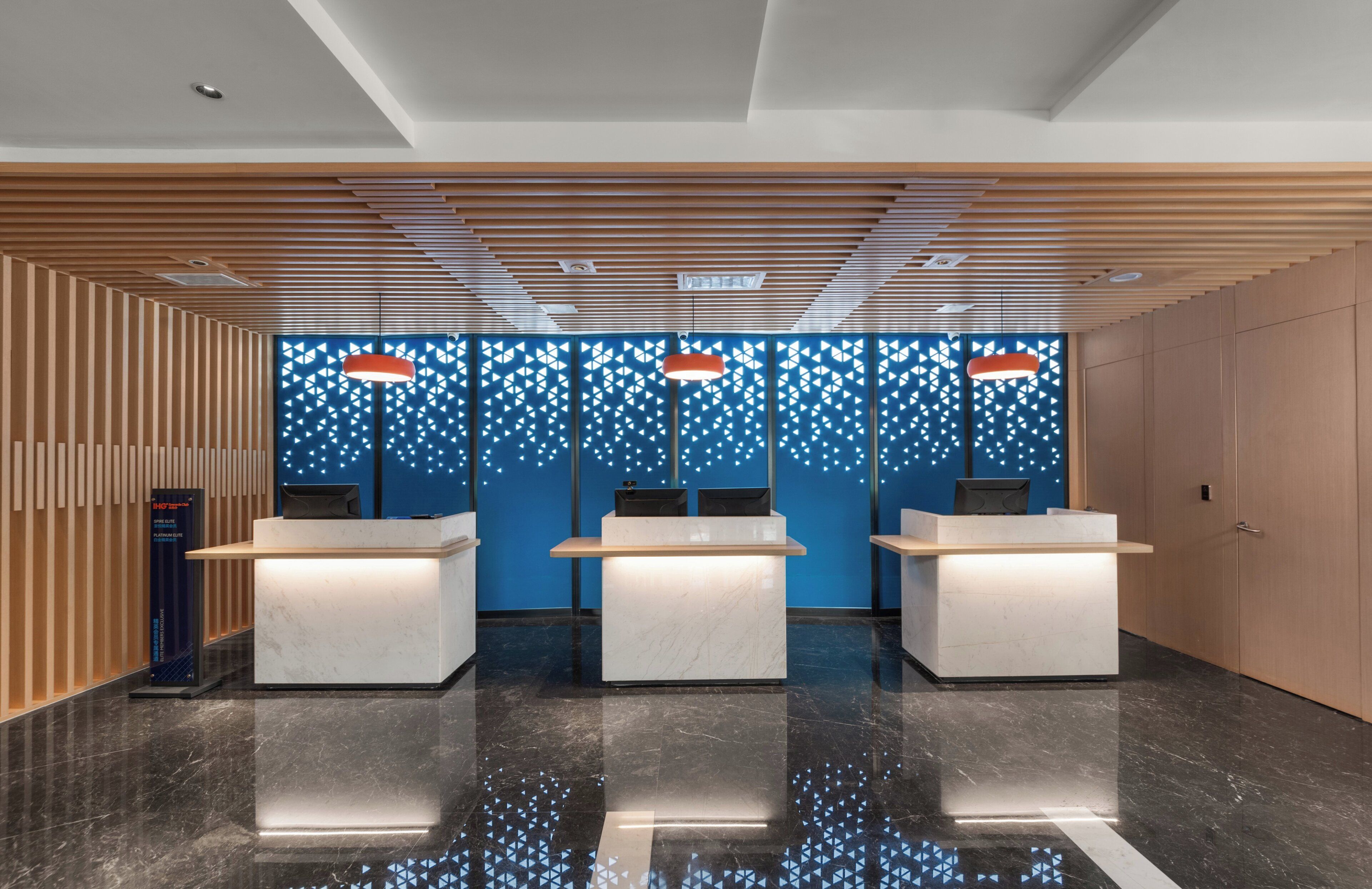 Zona de recepción con tres mostradores blancos, pared con diseño azul y techo de listones de madera.