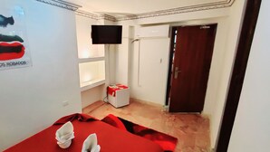 Een hotelkamer met een bed, een aan de muur bevestigde televisie, een deur en een poster.