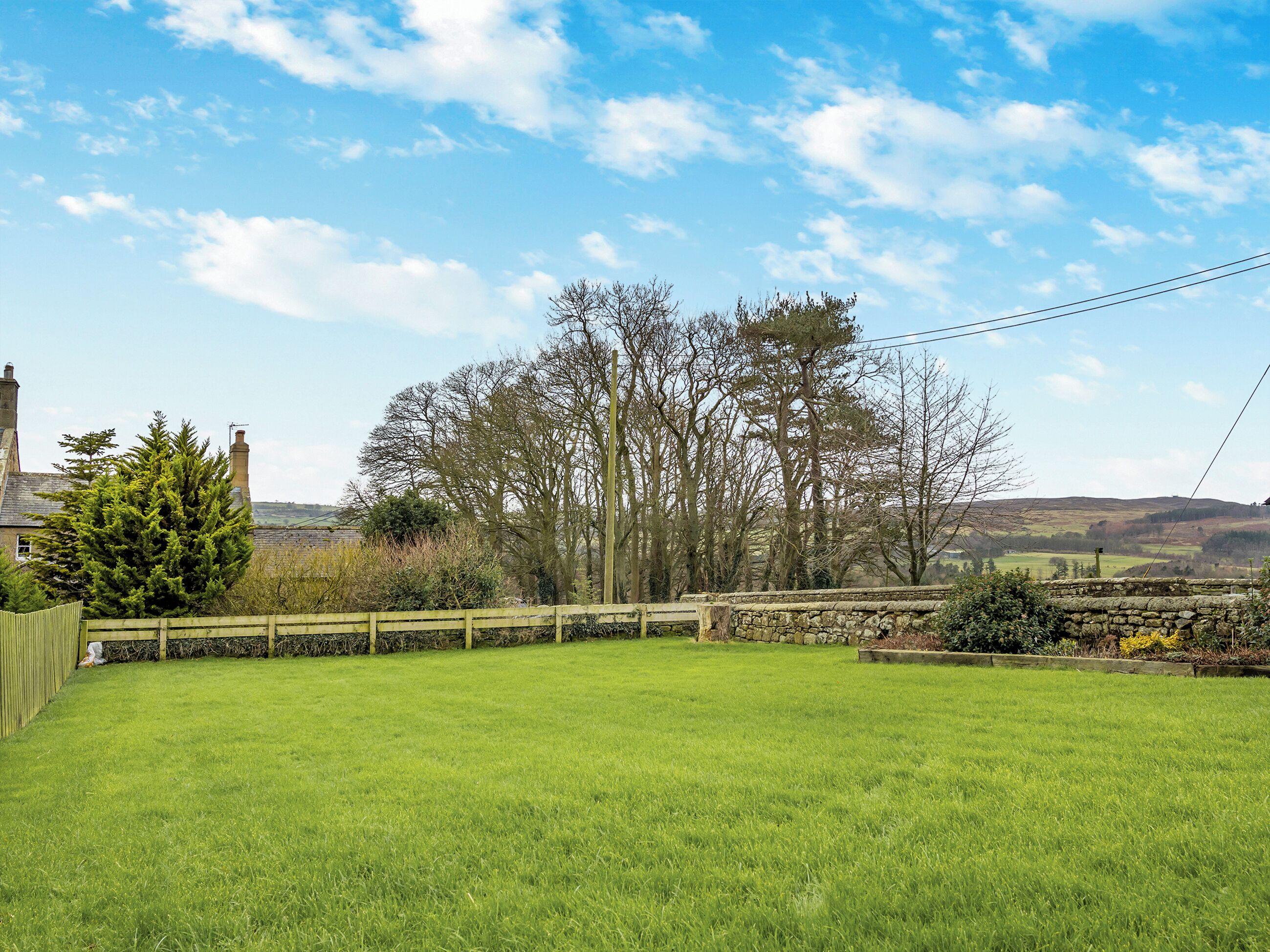 A grassy field with a stone wall and trees in the background.
