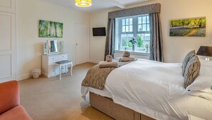 Ein Schlafzimmer mit Bett, Kommode, Fernseher und einem Fenster mit Vorhängen.