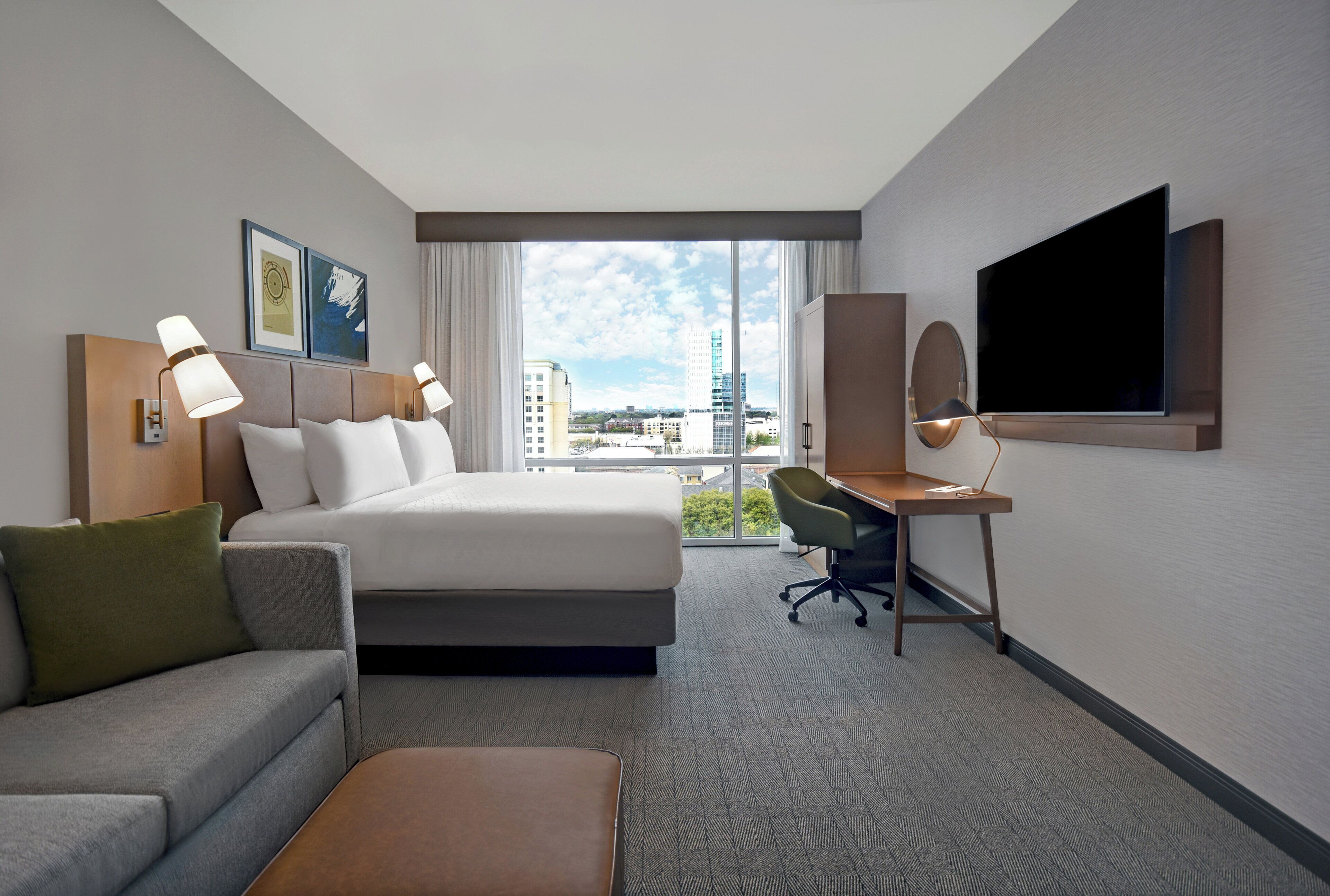 A hotel room with a bed, a desk, a television, and a view of the cityscape.