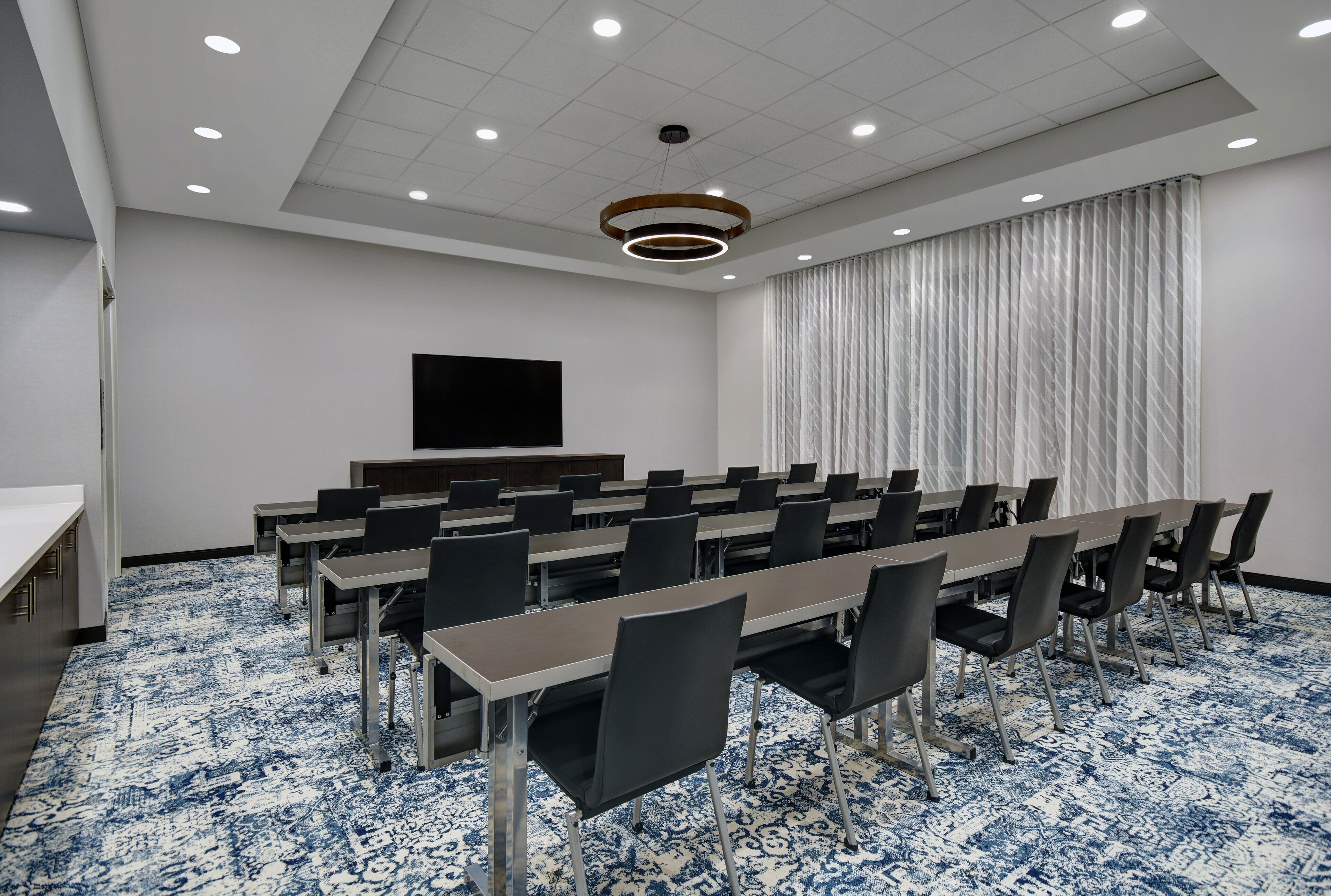 A conference room with a long table, chairs, a flat-screen TV, and a patterned carpet.