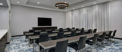 A conference room with a long table, chairs, a flat-screen TV, and a patterned carpet.