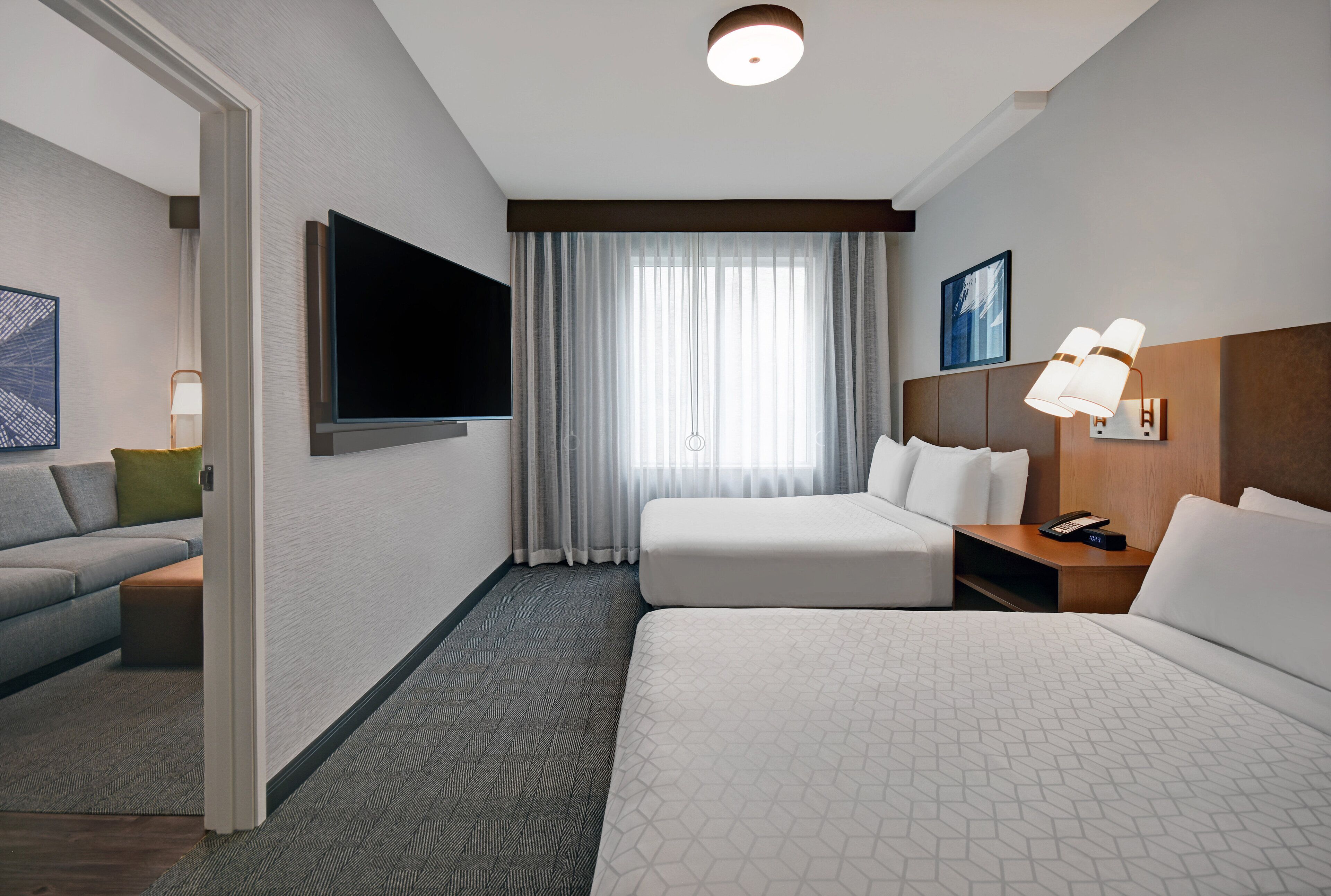 A hotel room with a bed, a sofa, a TV, a desk with a lamp, and a window with curtains.