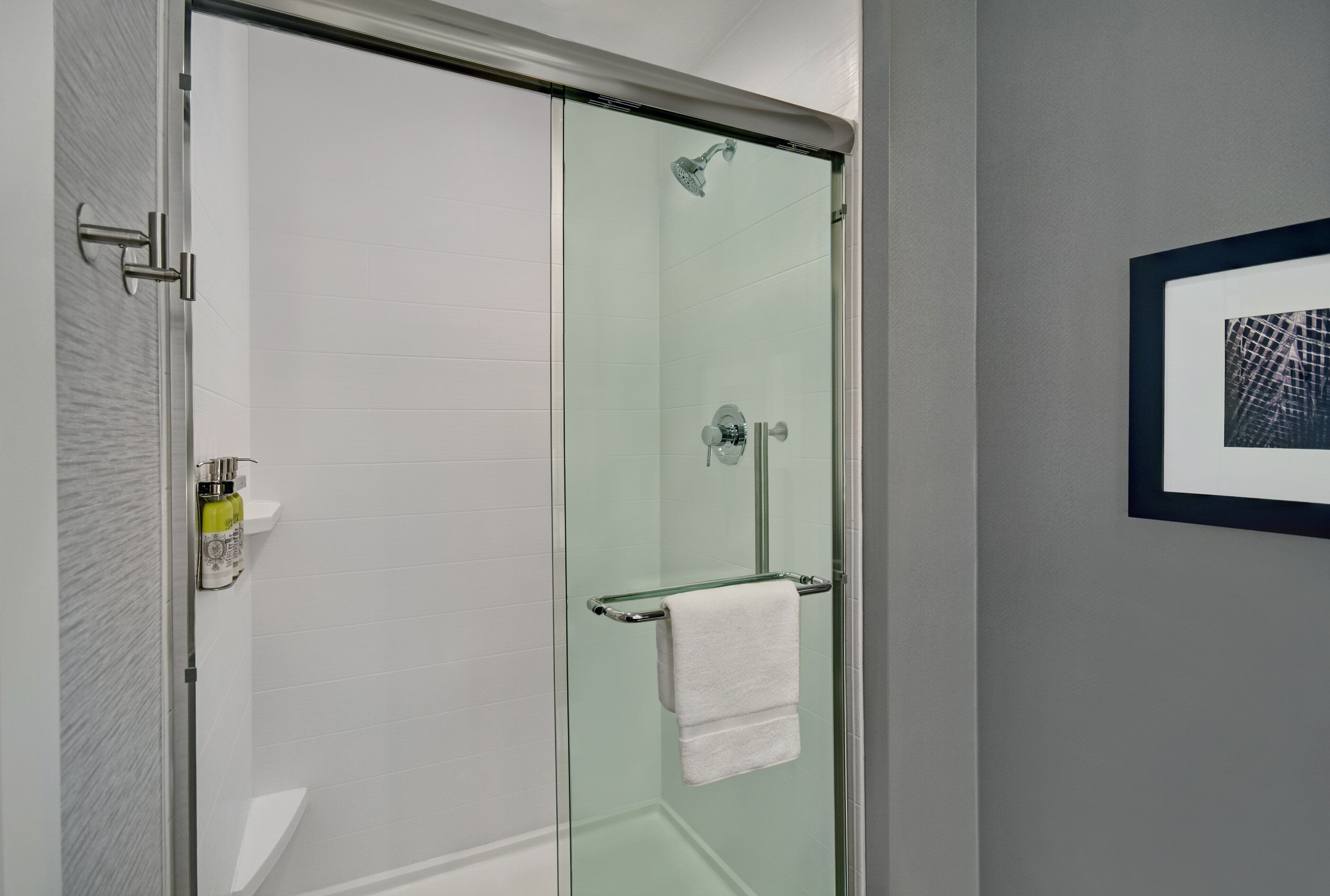 Un bagno moderno con box doccia in vetro, porta asciugamani in vetro e una cornice con un'immagine appesa al muro.