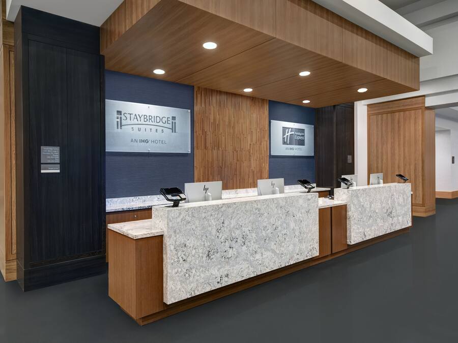 A reception desk with a marble top, wooden paneling, and two signs for Staybridge Suites Anhinga Hotel.
