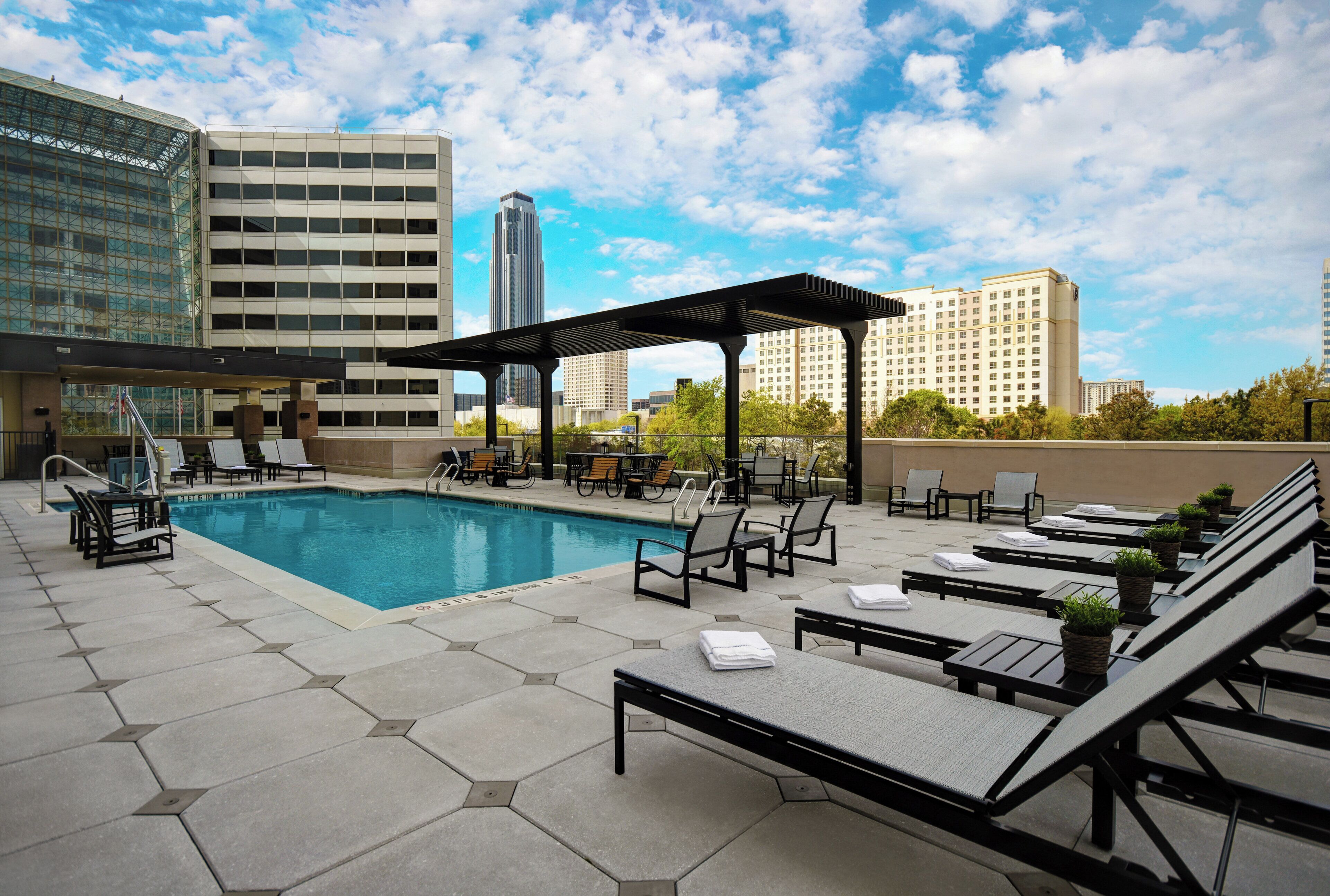 A rooftop pool area with lounge chairs and a pergola, surrounded by modern buildings.