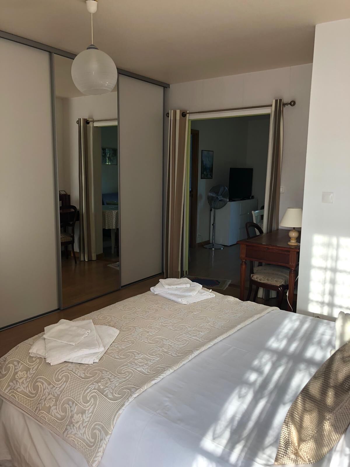 A hotel room with a large bed, a mirror, a desk, and a chair.