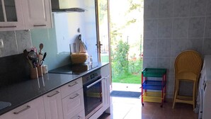 Une cuisine avec des meubles blancs, un plan de travail noir et un sol carrelé. Une fenêtre offre une vue sur la verdure à l’extérieur.