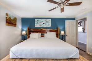 A bedroom with a large bed, a wooden headboard, two bedside lamps, and a ceiling fan.