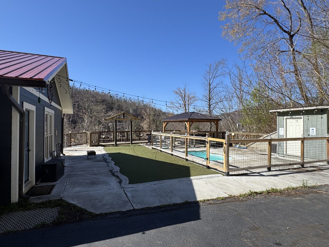 A backyard with a swimming pool, a covered patio, and a fenced play area.