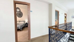A hotel corridor with a wooden door leading to a bedroom with a bed and a nightstand. - Gli Archi sul Mare (Gaeta)