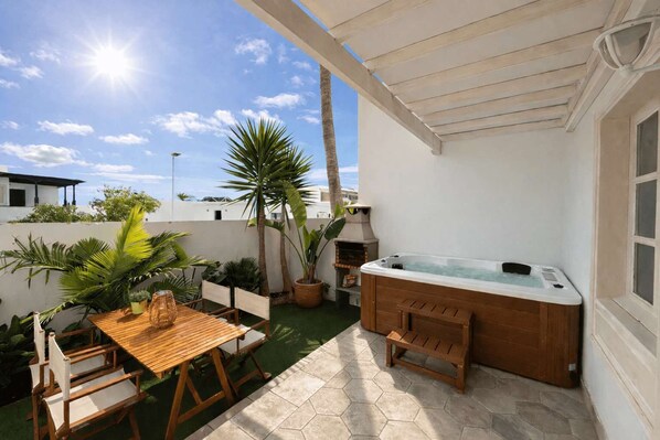 A patio with a wooden table and chairs, a hot tub, and potted plants.