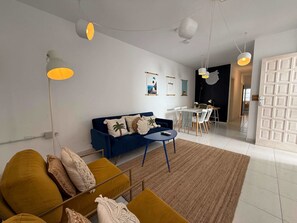A modern living room with a blue sofa, yellow armchairs, and a dining area with white chairs.