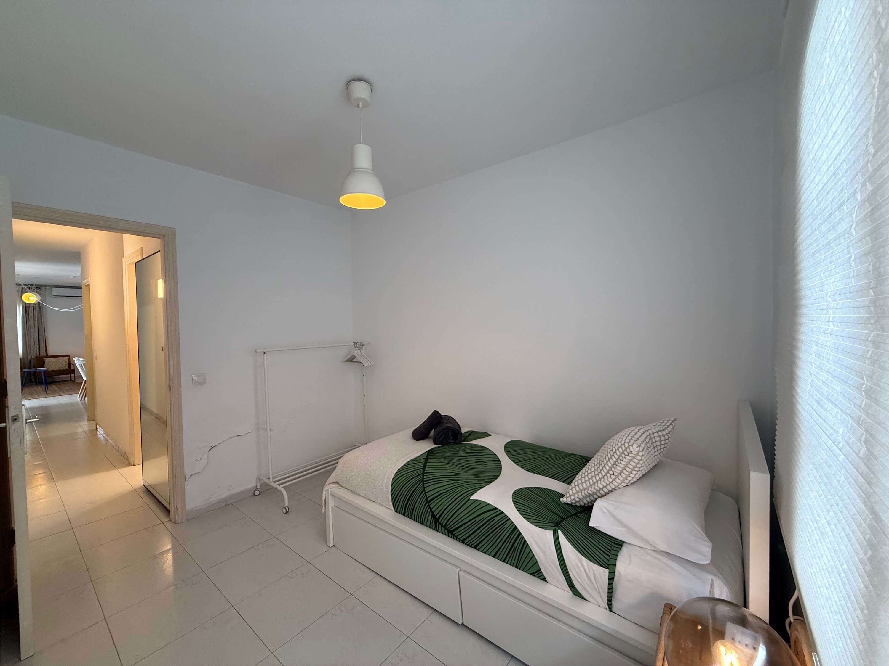 A bedroom with a bed, a hanging light fixture, a radiator, and a door leading to another room.