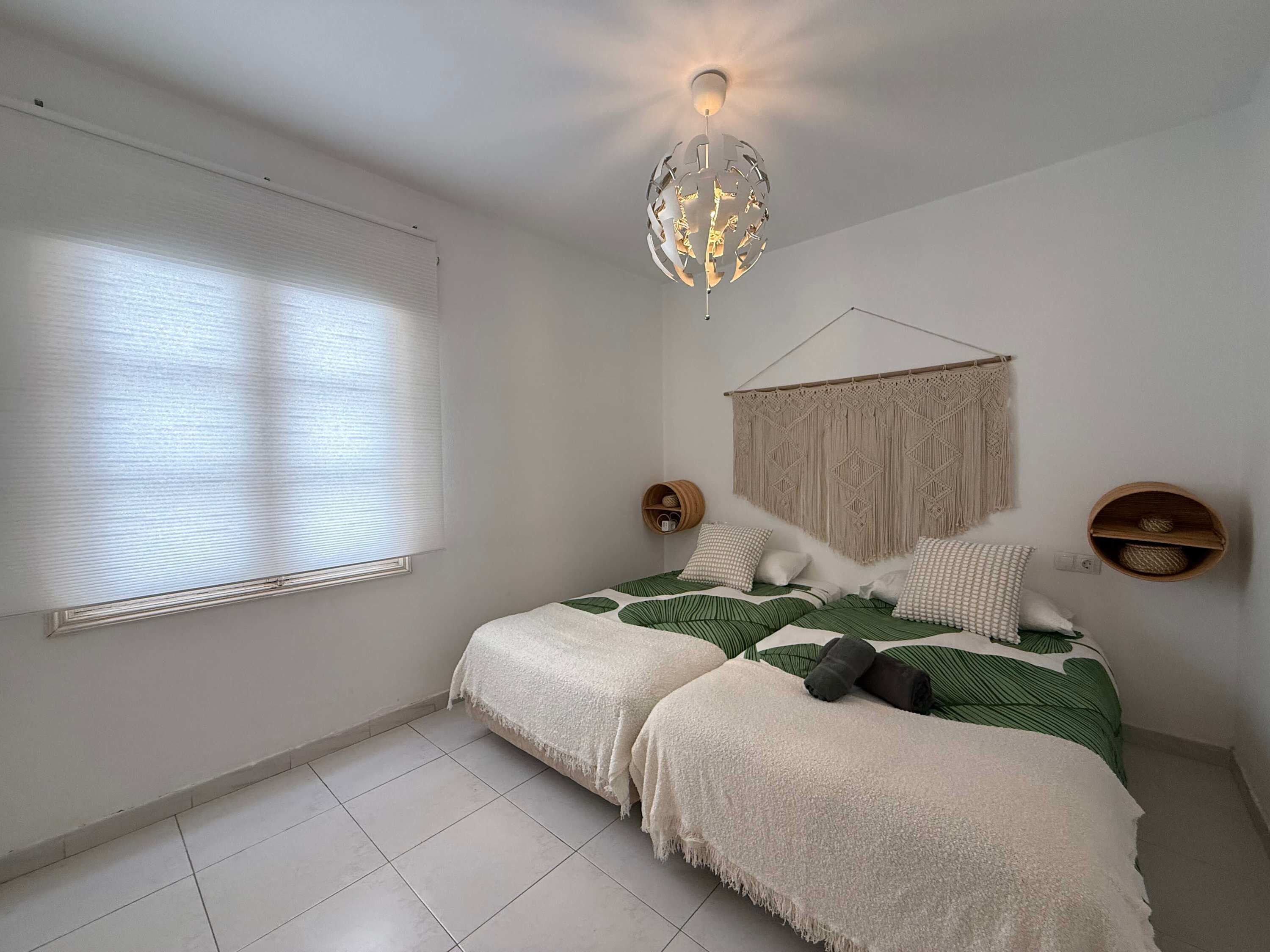 Una camera da letto con un letto, un arazzo in macramè e una lampada sferica particolare.