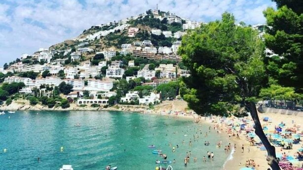 Uma vila costeira com edifícios numa encosta com vista para uma praia.