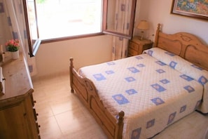 A bedroom with a wooden bed, a nightstand, a lamp, and a window with curtains.