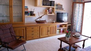 Uma sala de estar com um armário de madeira, televisão, estante e uma janela com cortinas.