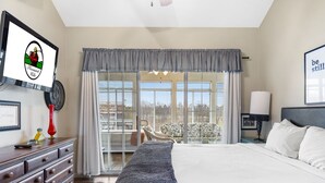 A hotel room with a large bed, a dresser, a TV, and a balcony with a view.