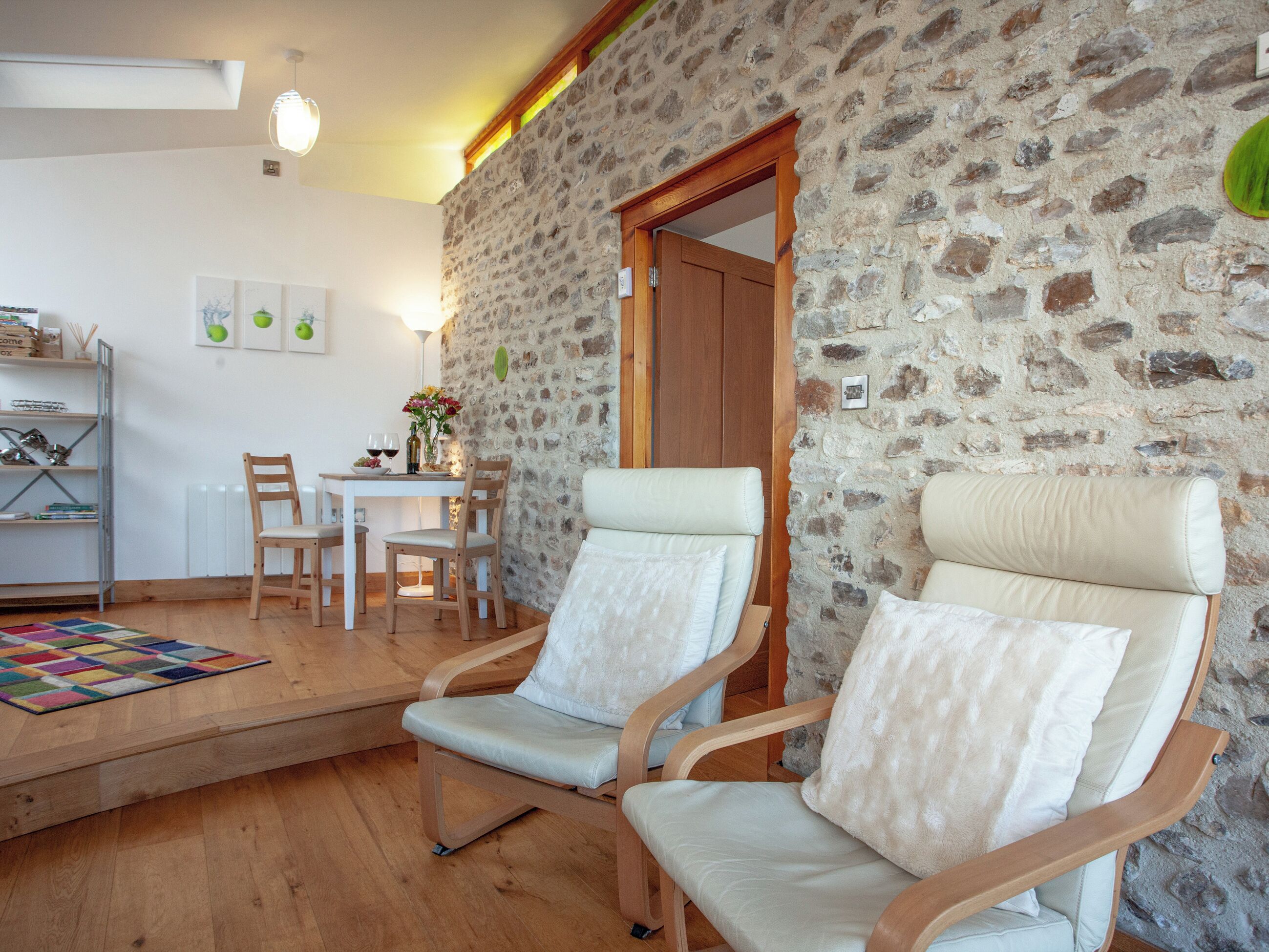 A cozy room with a stone wall, a wooden dining table with chairs, a sofa, and a bookshelf.