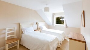 A bedroom with two beds, a wooden chair, a nightstand, a lamp, and a window with curtains. - House 3 Dingle Manor Remarkable 3-Bed House (Dingle)